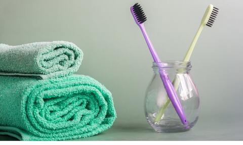 Green Towel Sit Next To Toothbrushes Stored In Multi-Purpose Glass Jars