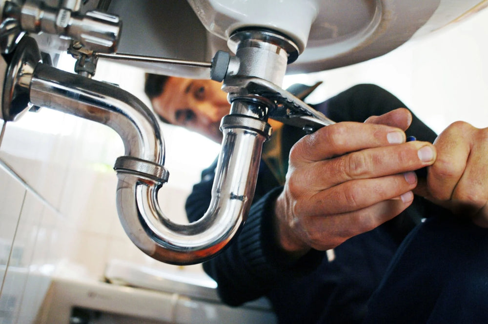 Plumber working on a sink with visible pipes and tools.