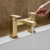 Close-up of the square brushed gold two-pillar bath filler tap running water into the bath