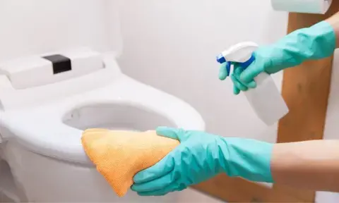 Man Hands Cleaning A Toilet Seat With Anti-Bacterial Spray and Microfiber Cloth