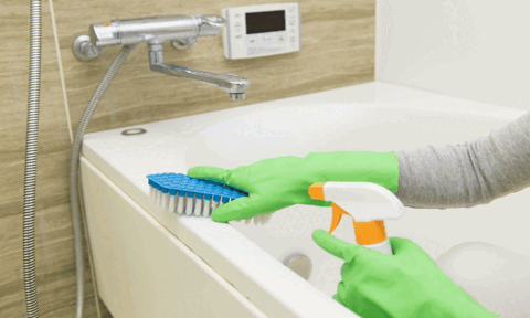 Man Deep Cleaning Bathtub Using Brush and Sprayer